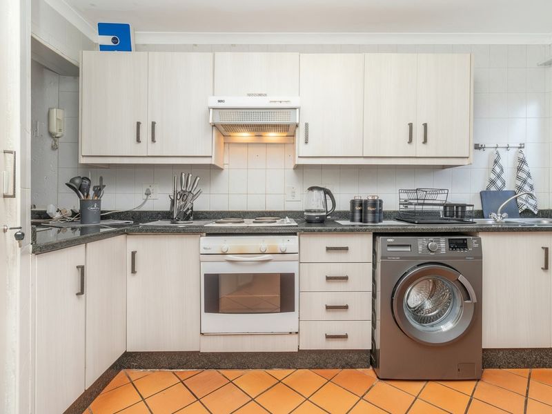 Functional kitchen featuring light-toned laminate cabinetry, granite countertops, built-in oven with extractor fan, and durable terracotta floor tiles.