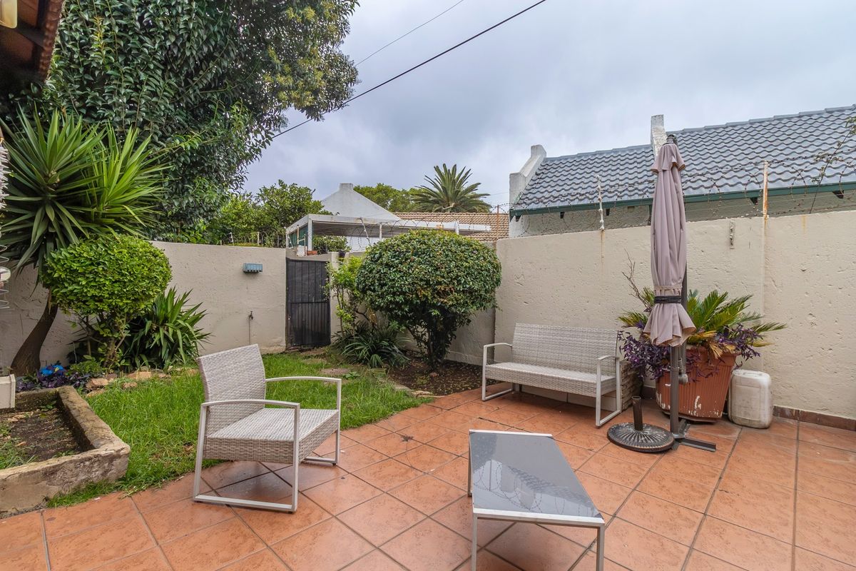 A private rear courtyard featuring a tiled patio area, perimeter boundary walls, and established garden landscaping.