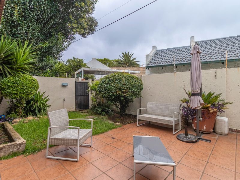 A private rear courtyard featuring a tiled patio area, perimeter boundary walls, and established garden landscaping.