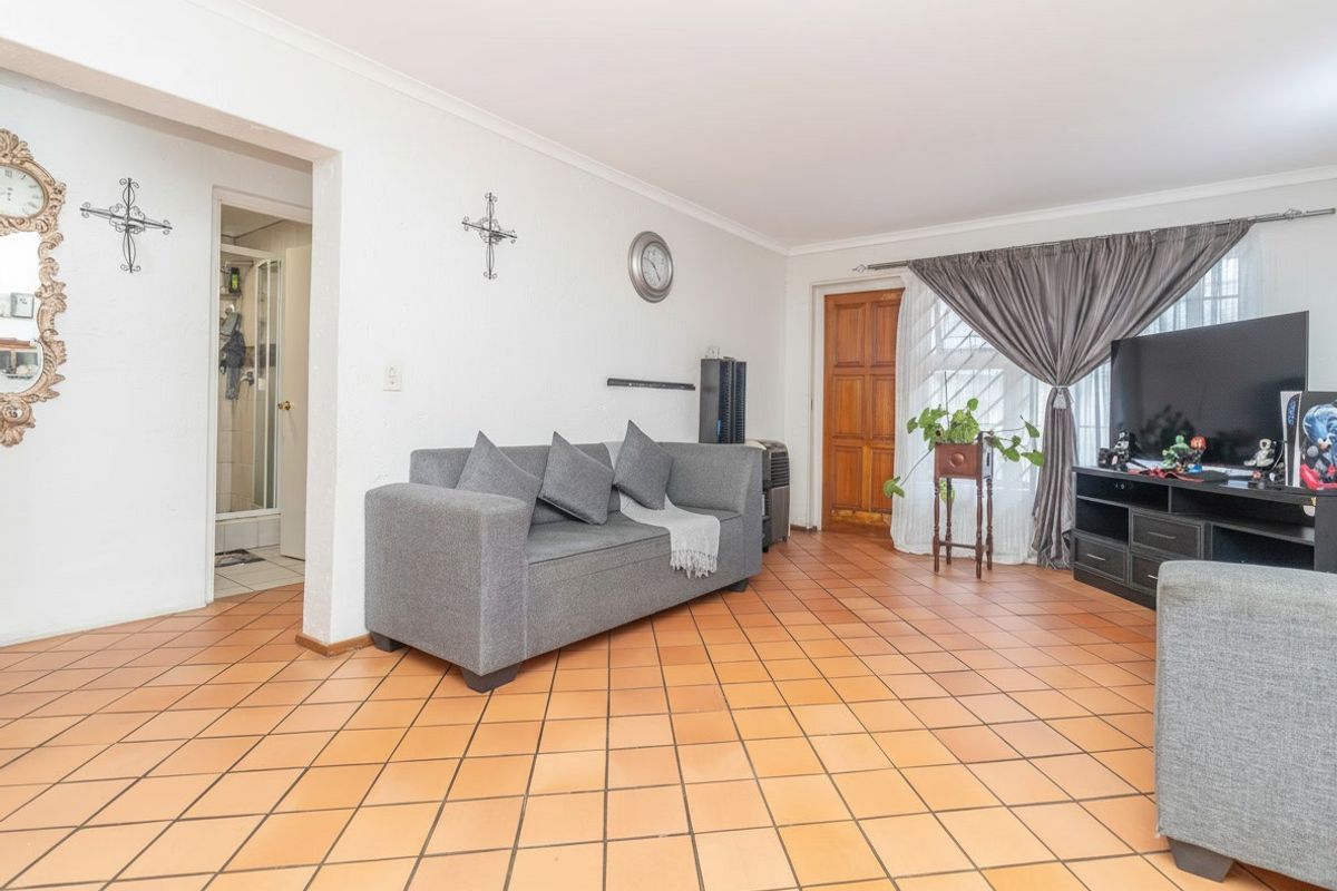 A spacious living room featuring traditional terracotta tiled flooring, coved ceilings, and direct access to an adjacent room.