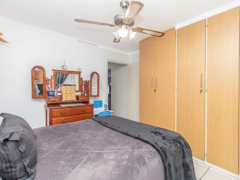 A bedroom featuring built-in wooden cupboards, a ceiling fan, and tiled flooring, offering a functional and well-maintained living space.