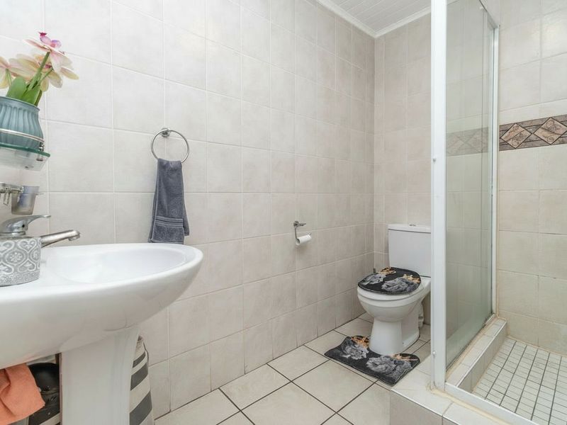 A functional bathroom featuring a pedestal basin, a tiled shower enclosure, and a standard toilet with neutral wall and floor tiling.