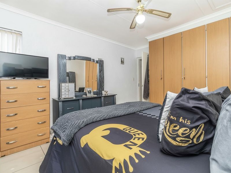 A bedroom featuring built-in wooden cupboards, a ceiling fan, and tiled flooring, offering a functional and well-maintained living space.