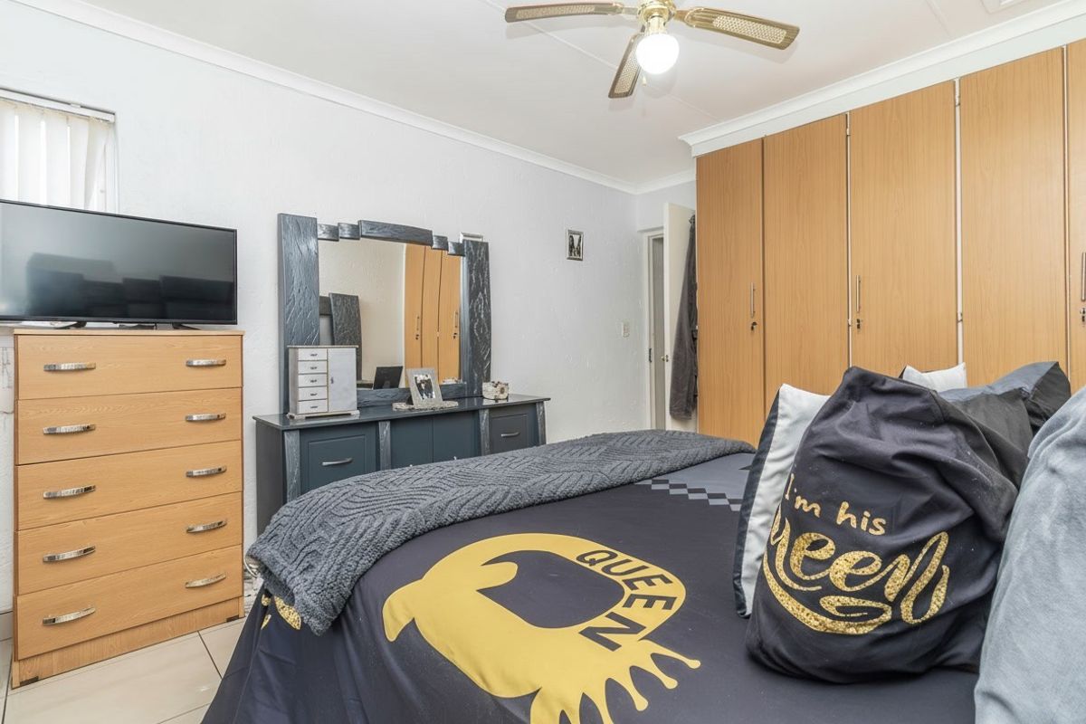 A bedroom featuring built-in wooden cupboards, a ceiling fan, and tiled flooring, offering a functional and well-maintained living space.