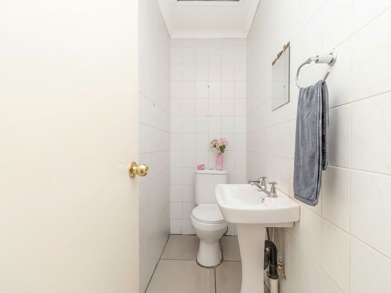 A compact guest bathroom featuring a pedestal sink, toilet, and fully tiled walls and flooring.
