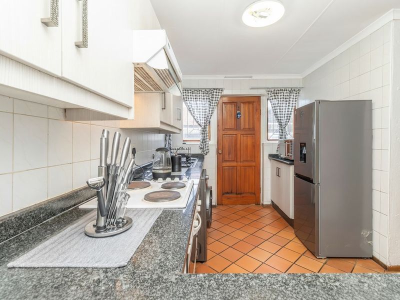 A functional kitchen featuring granite countertops, an electric hob with extractor fan, tiled flooring, and classic cabinetry with a solid wood rear door.