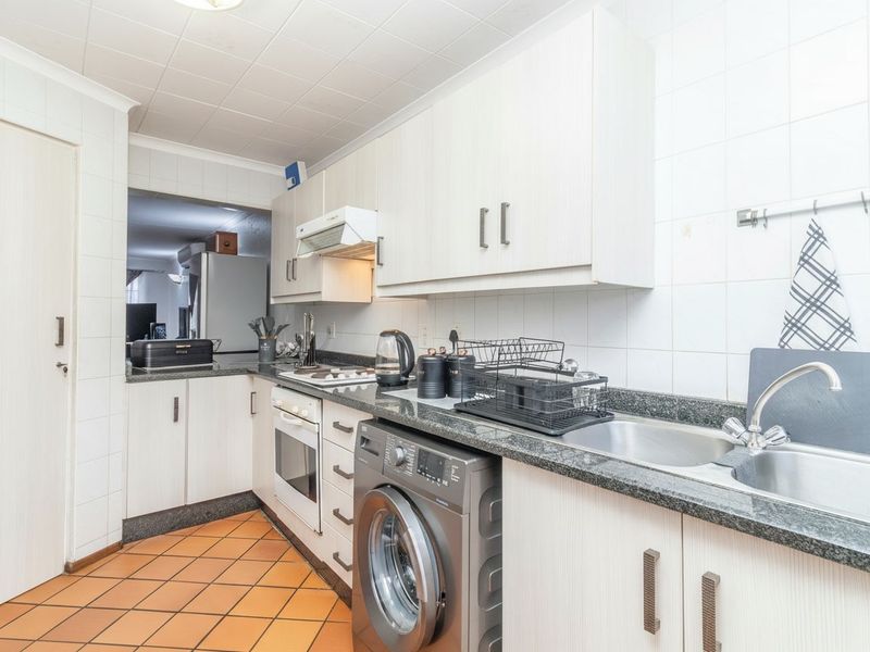 A functional kitchen featuring built-in cabinetry, granite countertops, a stainless steel sink, and integrated appliances with tiled finishes throughout.
