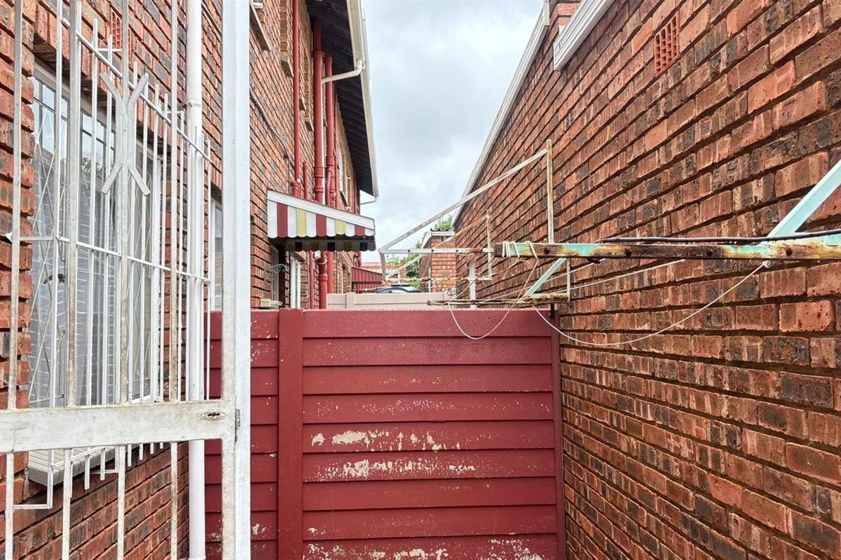 A narrow exterior rear service area featuring brick walls, a fixed washing line, and a small awning.