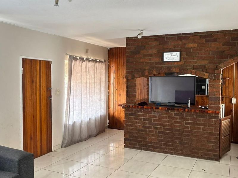 Living room featuring a prominent brick fireplace, tiled flooring, and wooden wall paneling, offering a dated aesthetic with potential for modernization.