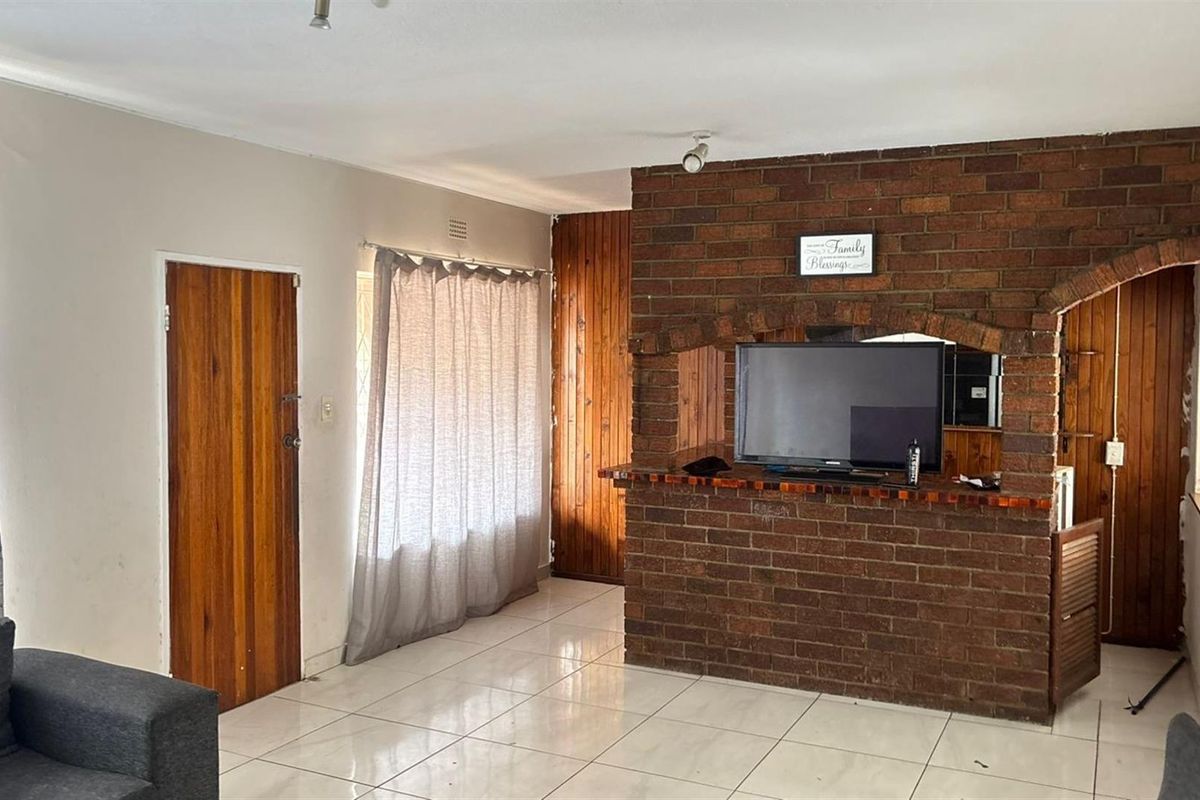 Living room featuring a prominent brick fireplace, tiled flooring, and wooden wall paneling, offering a dated aesthetic with potential for modernization.