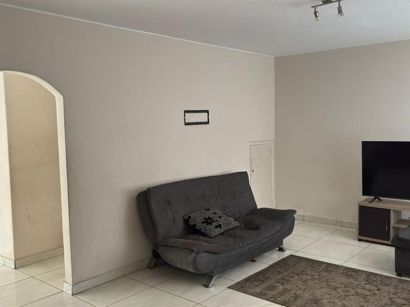 A living room featuring tiled flooring and an arched entryway, providing a neutral base for potential interior updates.