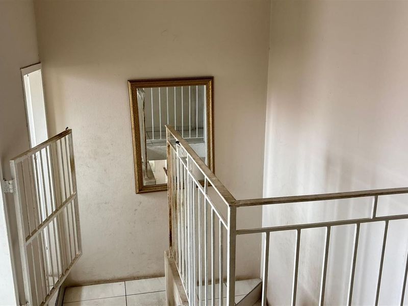 A stairwell area featuring tiled flooring and a metal balustrade, showing signs of wear on the walls and railing.