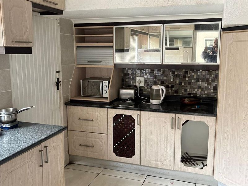 A dated kitchen featuring laminate cabinetry, granite countertops, and a mosaic tile backsplash, currently showing signs of wear and missing cabinet components.