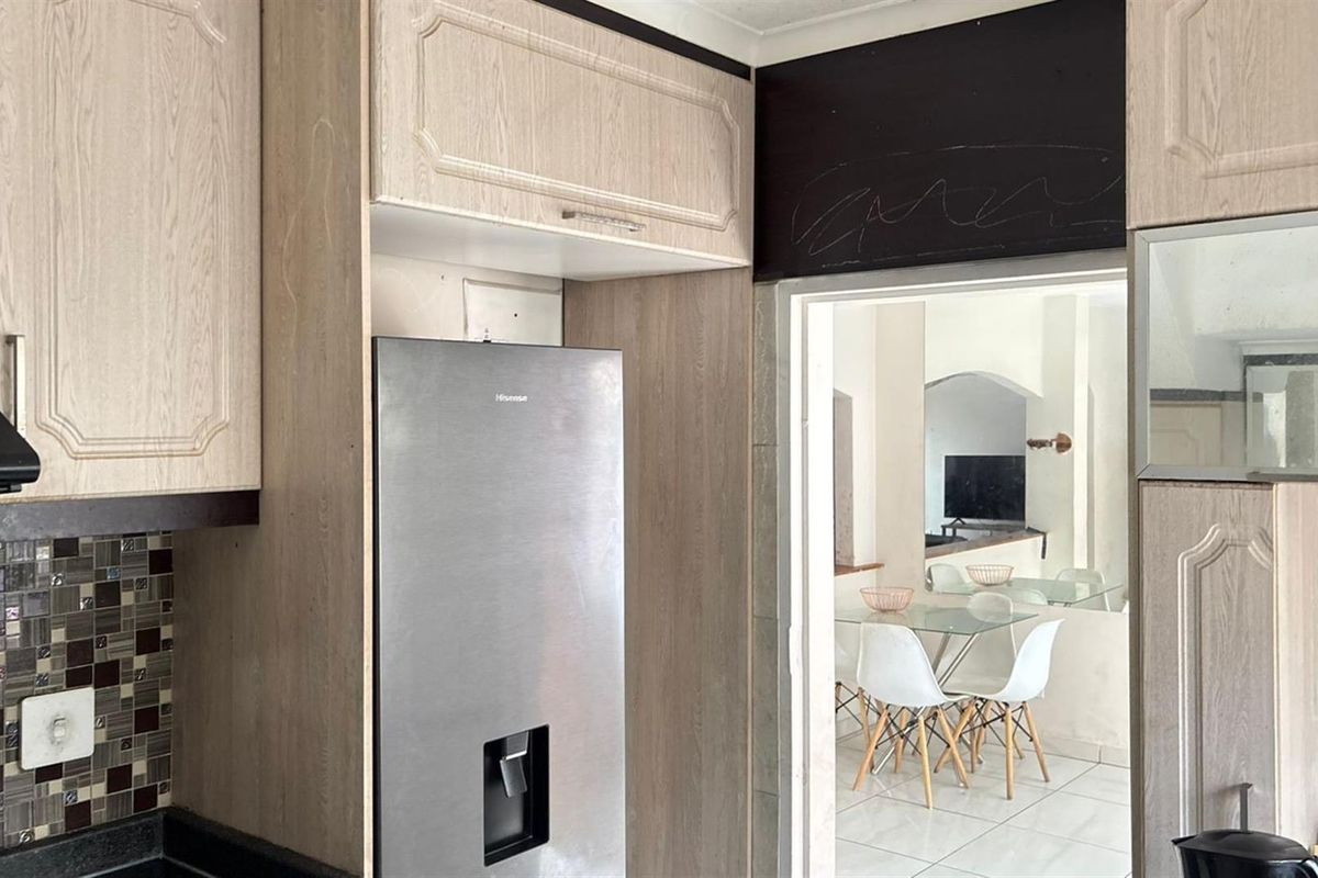 Kitchen featuring light wood-look cabinetry, mosaic tile backsplash, and stone countertops, with a direct view into the adjacent dining area.