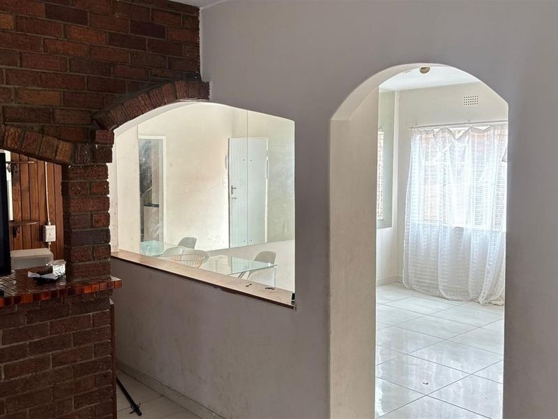 Open plan living area featuring a brick accent wall, arched architectural details, and tiled flooring connecting to an adjacent room.
