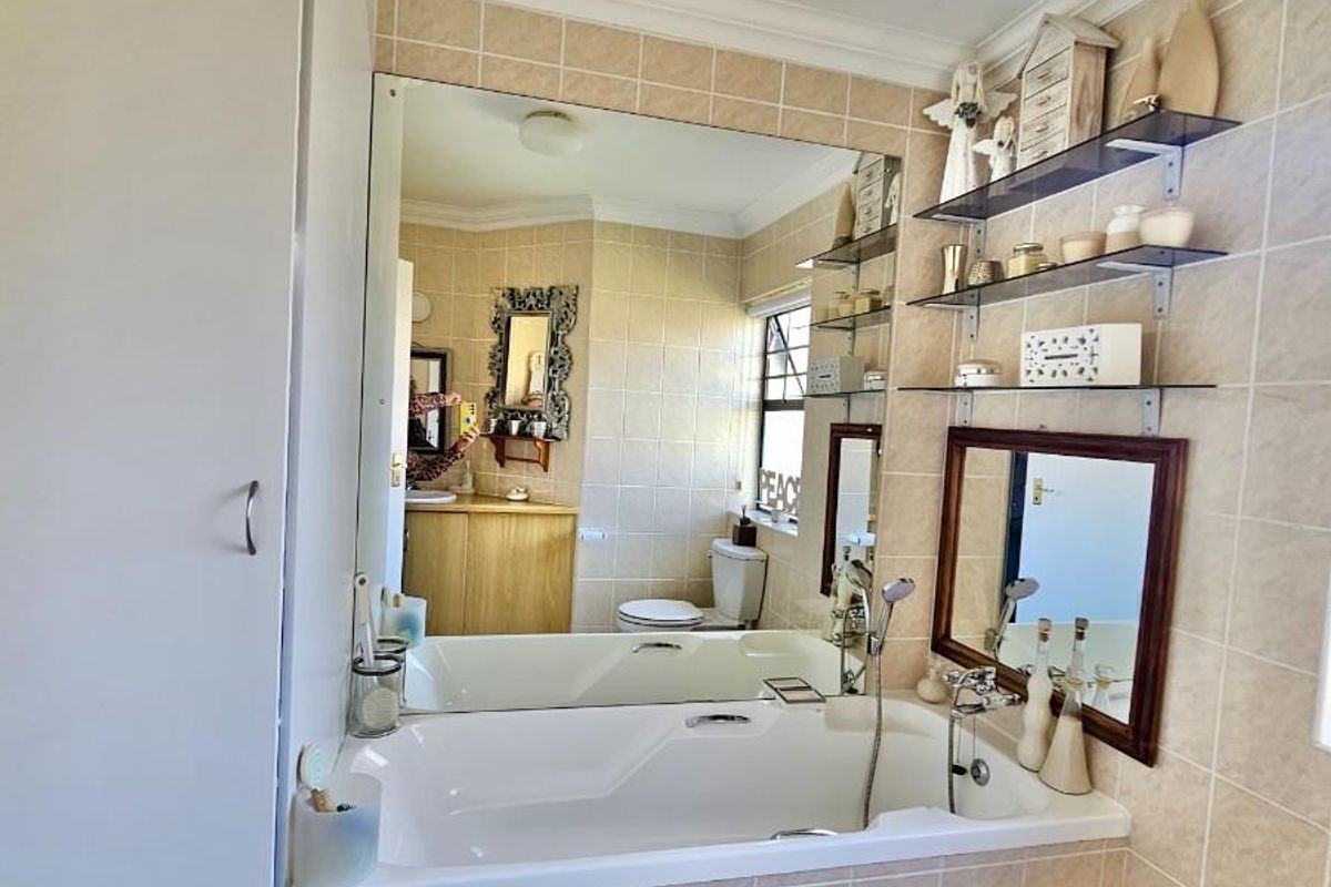 A functional bathroom featuring a built-in bathtub with shower mixer, large wall-mounted mirror, and tiled wall finishes.