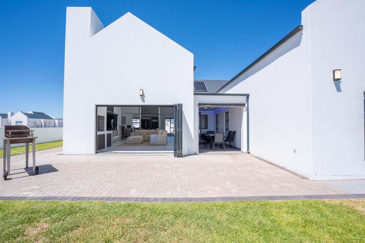 A modern rear exterior view featuring a paved patio area, seamless indoor-outdoor flow through folding doors, and a covered entertainment space.