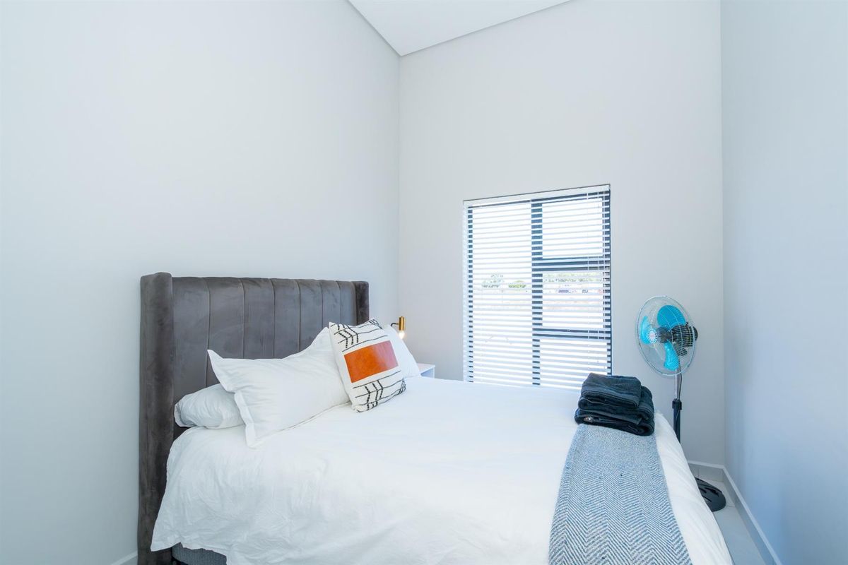 A bright and modern bedroom featuring high ceilings, neutral walls, and a large window fitted with horizontal blinds.