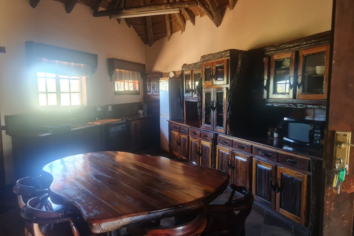 Rustic kitchen featuring custom dark wood cabinetry, a high thatched ceiling with exposed timber beams, and a large integrated dining area.