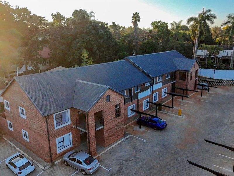 Aerial view of a multi-story face brick townhouse complex featuring a corrugated metal roof and dedicated paved parking bays with carports.