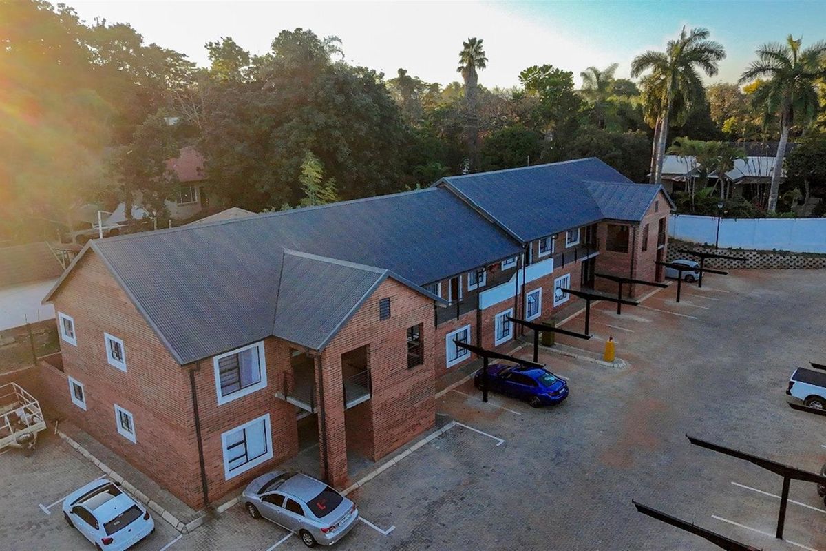 Aerial view of a multi-story face brick townhouse complex featuring a corrugated metal roof and dedicated paved parking bays with carports.