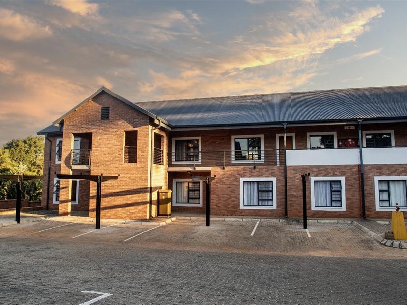 A well-maintained townhouse complex featuring a face brick facade, corrugated metal roofing, and dedicated paved parking bays with covered structures.