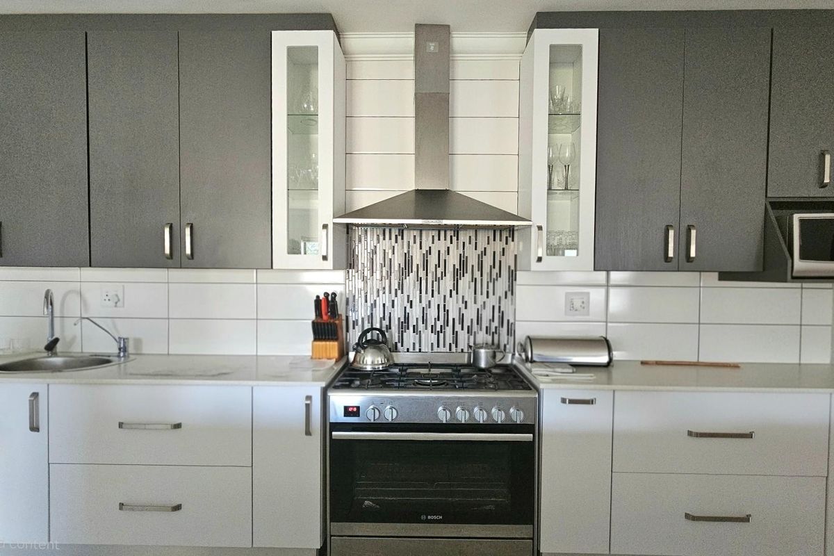 Modern kitchen featuring two-tone cabinetry, stainless steel gas stove with extractor fan, mosaic tile splashback, and integrated microwave.
