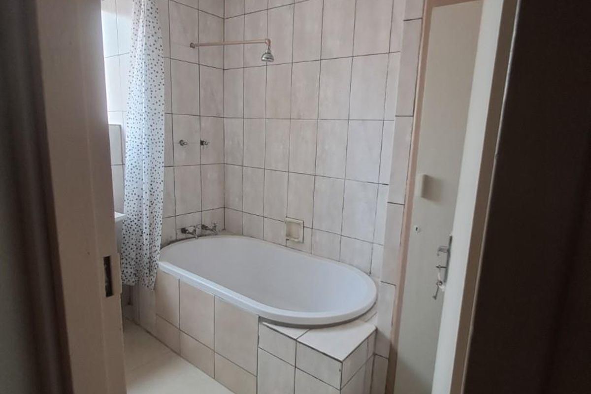A functional bathroom featuring a built-in bathtub with shower overhead, tiled walls, and integrated storage cabinetry.