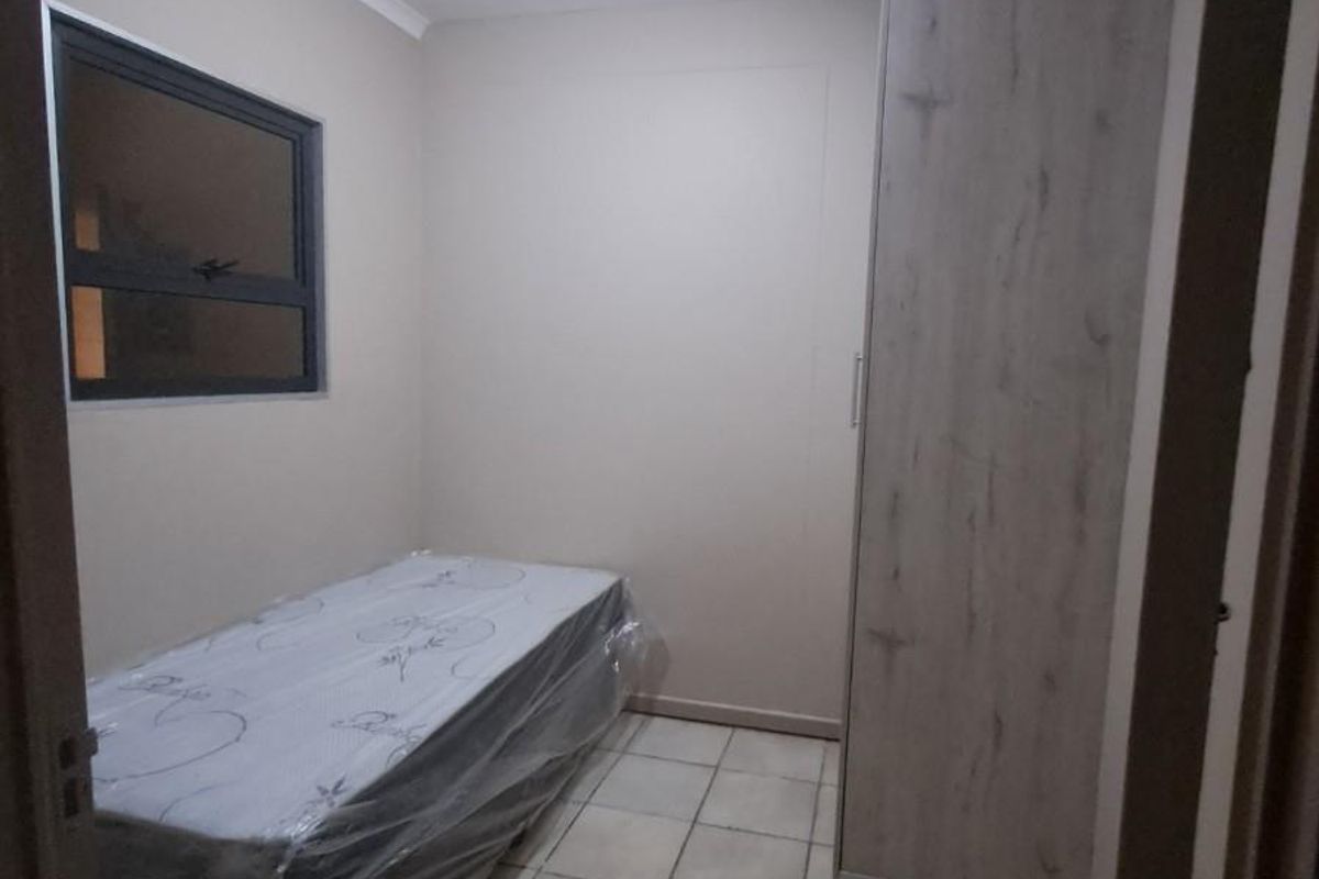 A compact bedroom featuring tiled flooring, a built-in wardrobe with a wood-grain finish, and a window with a dark frame.