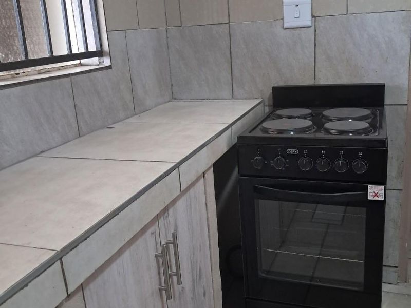 A functional kitchen area featuring tiled countertops, built-in cabinetry, and a freestanding electric stove with a four-plate hob.