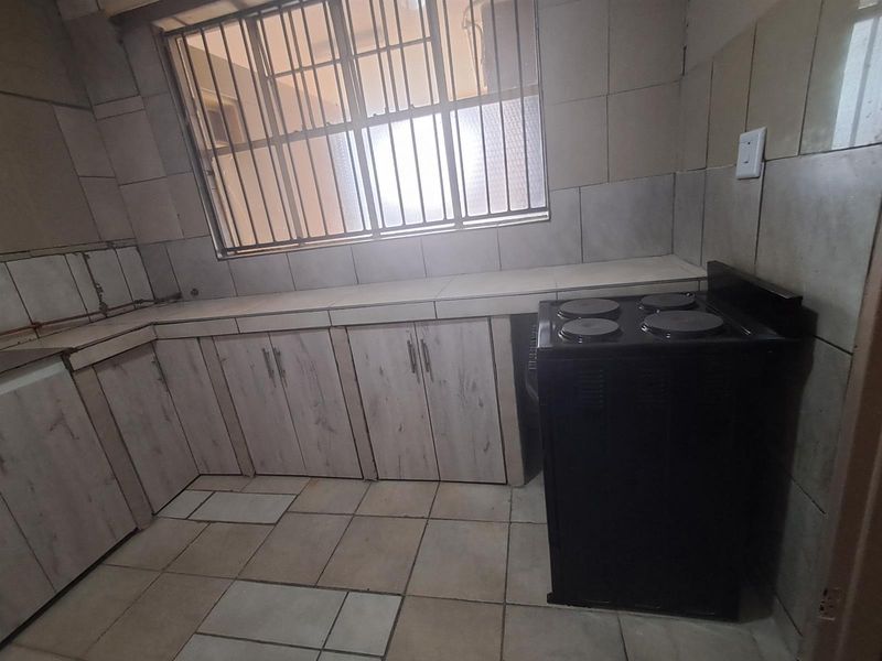 A functional kitchen area featuring tiled flooring, built-in cabinetry, and a freestanding electric stove, with a window providing natural light.