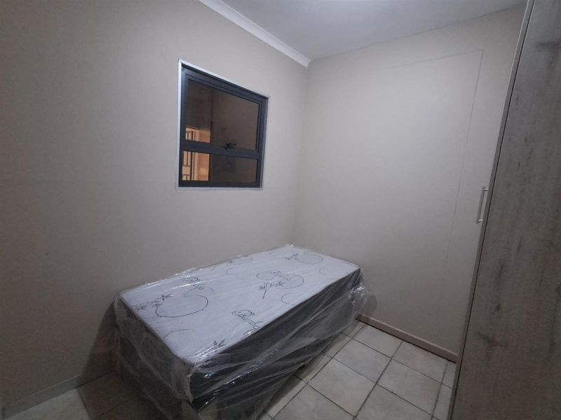 A compact bedroom featuring tiled flooring, neutral wall finishes, and a built-in cupboard.