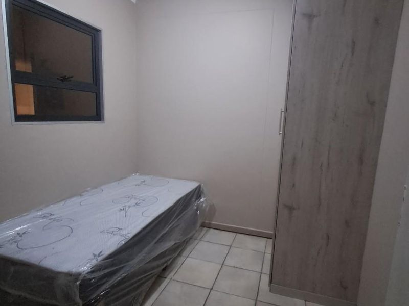 A compact bedroom featuring tiled flooring, a built-in wooden wardrobe, and a window, providing a functional and neutral living space.