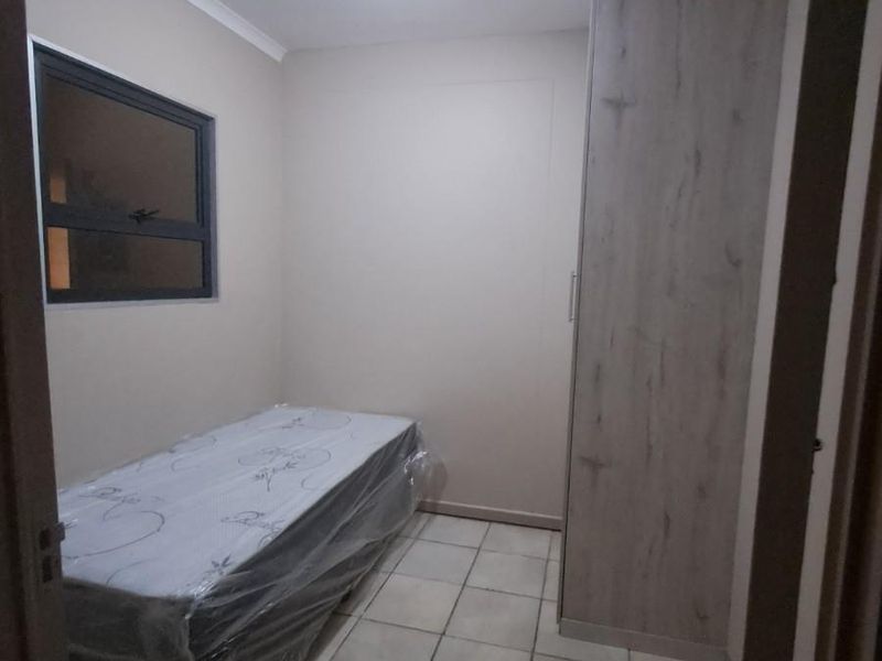 A compact bedroom featuring tiled flooring, a built-in wardrobe with a wood-grain finish, and a window with a dark frame.