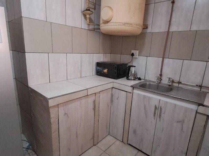 A compact kitchen area featuring tiled surfaces, built-in cabinetry, a stainless steel sink, and an exposed wall-mounted water heater.