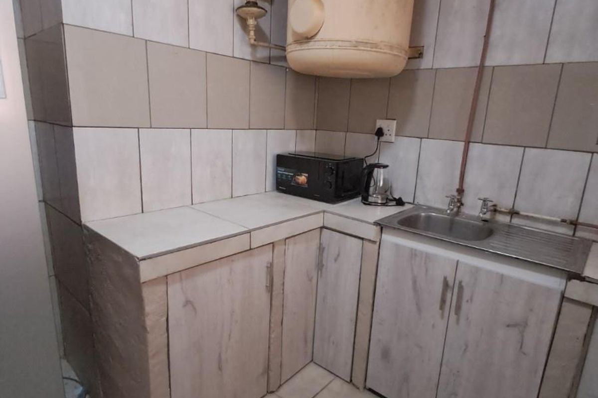 A compact kitchen area featuring tiled surfaces, built-in cabinetry, a stainless steel sink, and an exposed wall-mounted water heater.