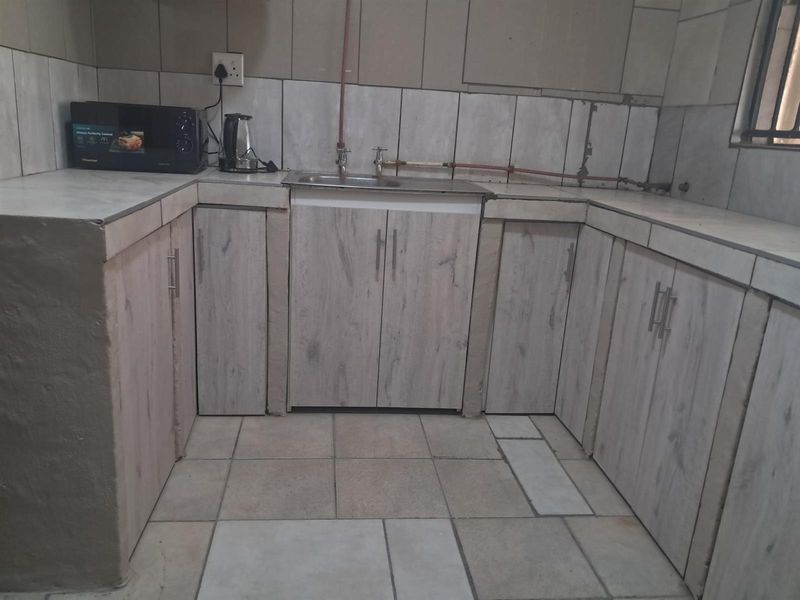 A functional kitchen area featuring light wood-look cabinetry, tiled flooring, and exposed plumbing fixtures along the backsplash.
