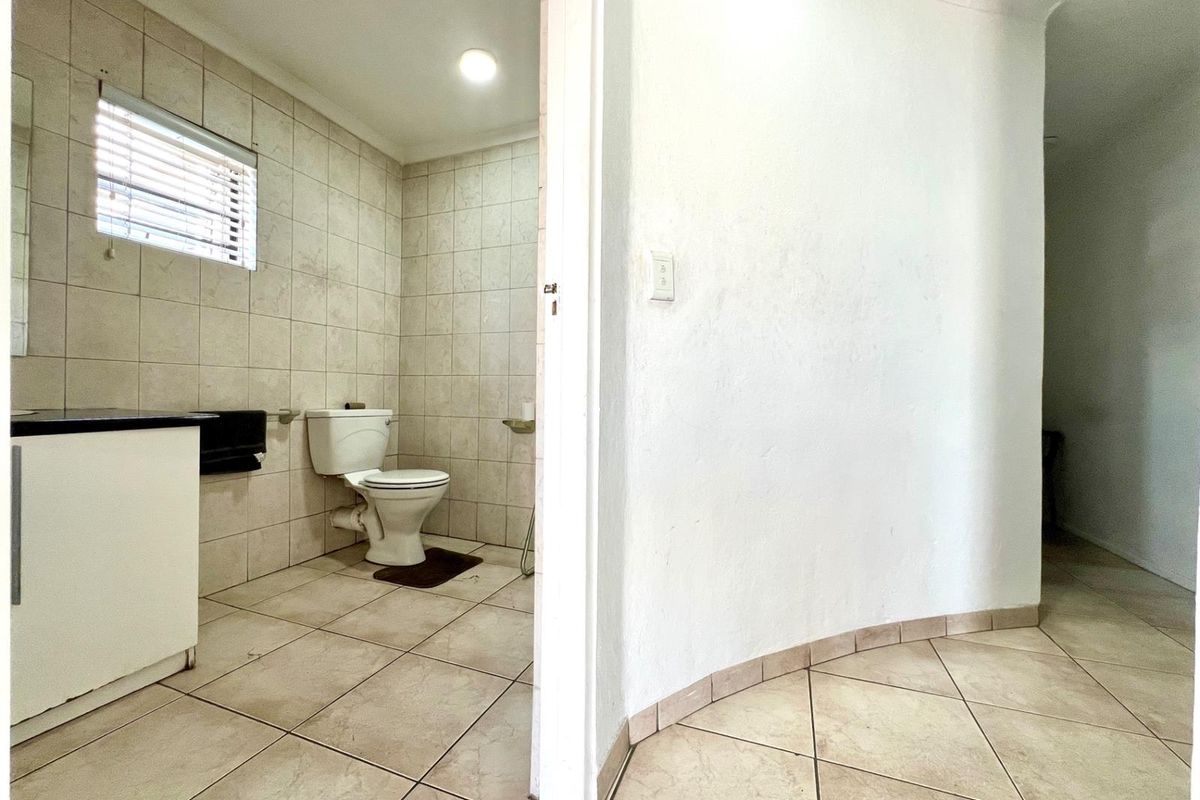 A functional bathroom featuring tiled walls and flooring, a built-in vanity, and a standard toilet, viewed from an adjacent hallway.