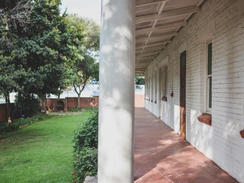 A covered veranda featuring a painted brick facade, support columns, and a timber roof structure, overlooking a private garden area.