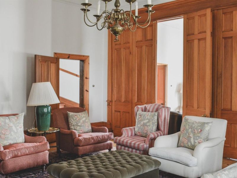 A classic living room featuring elegant timber paneling, solid wood doors, and a traditional brass chandelier, showcasing high-quality architectural craftsmanship.