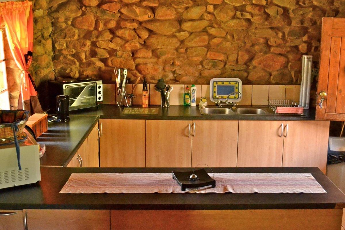 Rustic kitchen featuring exposed natural stone walling, laminate countertops, and wooden cabinetry, offering a warm and traditional farm-style aesthetic.