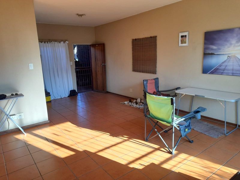 A spacious living area featuring ceramic floor tiles, a timber entrance door, and a security gate, offering a blank canvas for interior design.