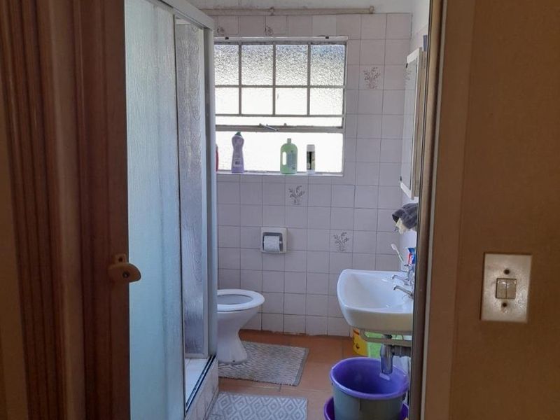 A compact bathroom featuring a shower enclosure, wall-mounted basin, and toilet, with tiled finishes throughout. The space requires cosmetic updates and maintenance.
