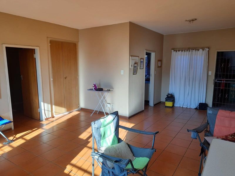 A spacious living area featuring neutral wall tones, ceramic floor tiles, and built-in storage cupboards, offering a versatile layout for various furniture arrangements.