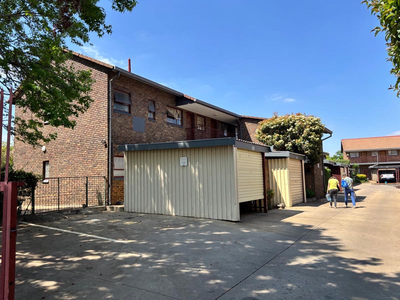 Exterior view of a face brick apartment complex featuring metal garage units and a concrete driveway area.