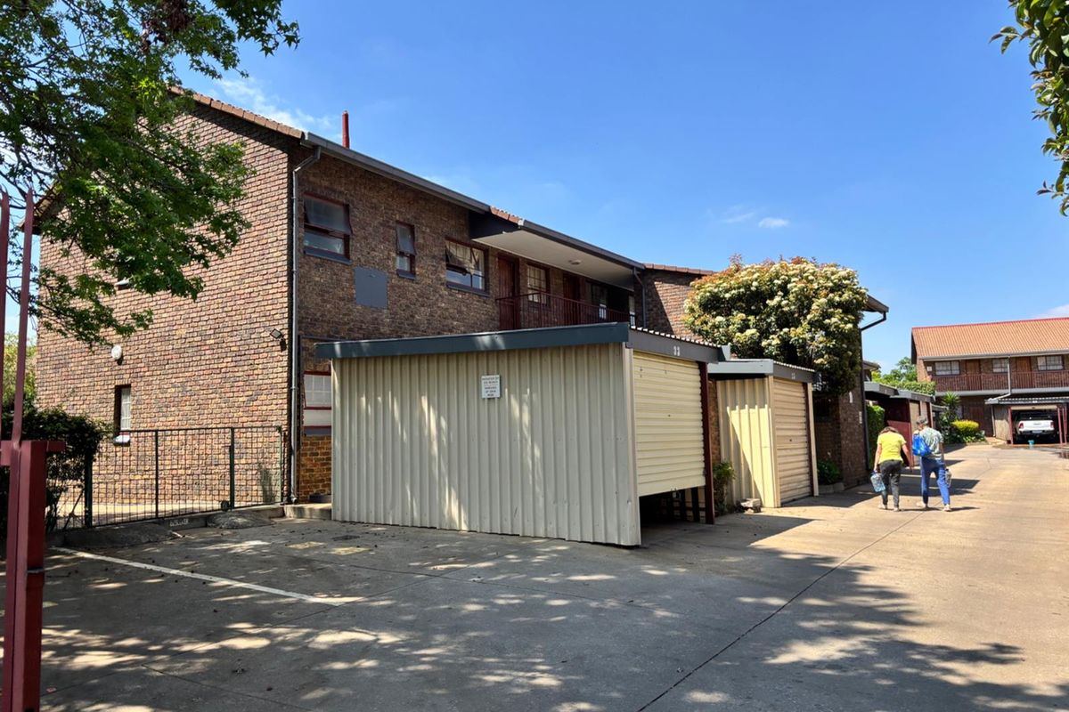 Exterior view of a face brick apartment complex featuring metal garage units and a concrete driveway area.
