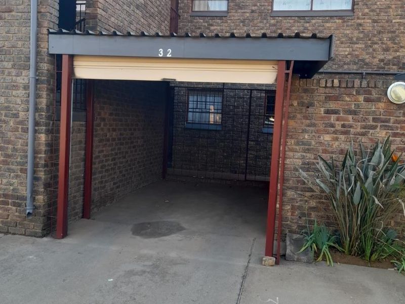 A covered carport area featuring brick exterior walls, concrete flooring, and security bars on the windows.