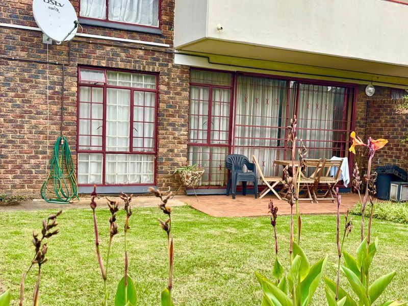 A rear view of the apartment featuring a private garden, a small terracotta patio area, and brick exterior walls with security bars on windows.