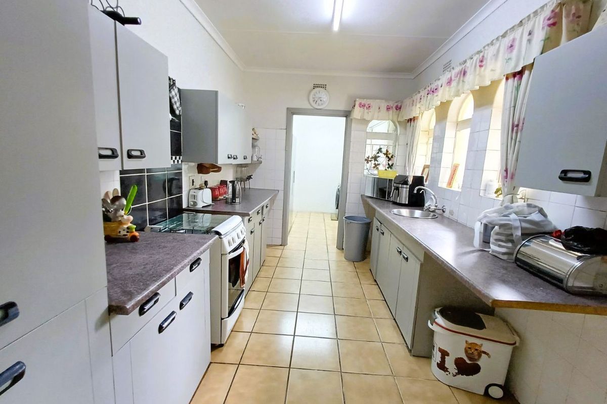 A functional galley-style kitchen featuring laminate countertops, tiled flooring, built-in cabinetry, and a freestanding stove, offering a practical layout for daily meal preparation.