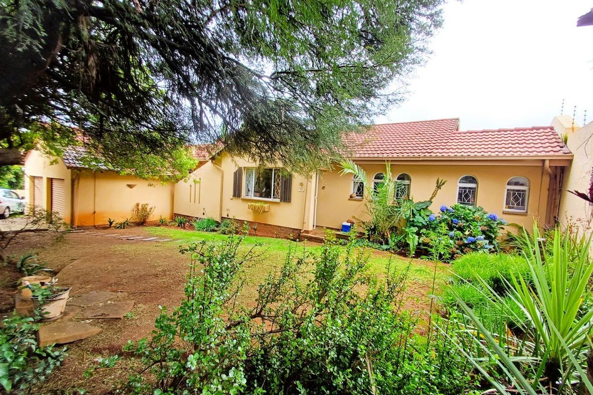 Rear view of a single-story house featuring a tiled roof, arched windows, and a landscaped garden area.